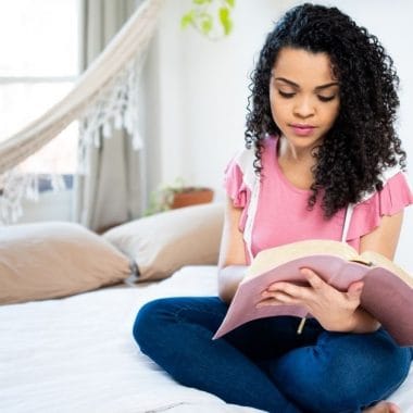 Young woman sitting on her bed, reading the bible